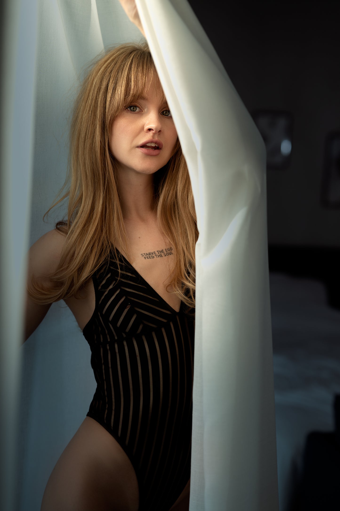 Woman in a black swimsuit peeking from behind white curtains